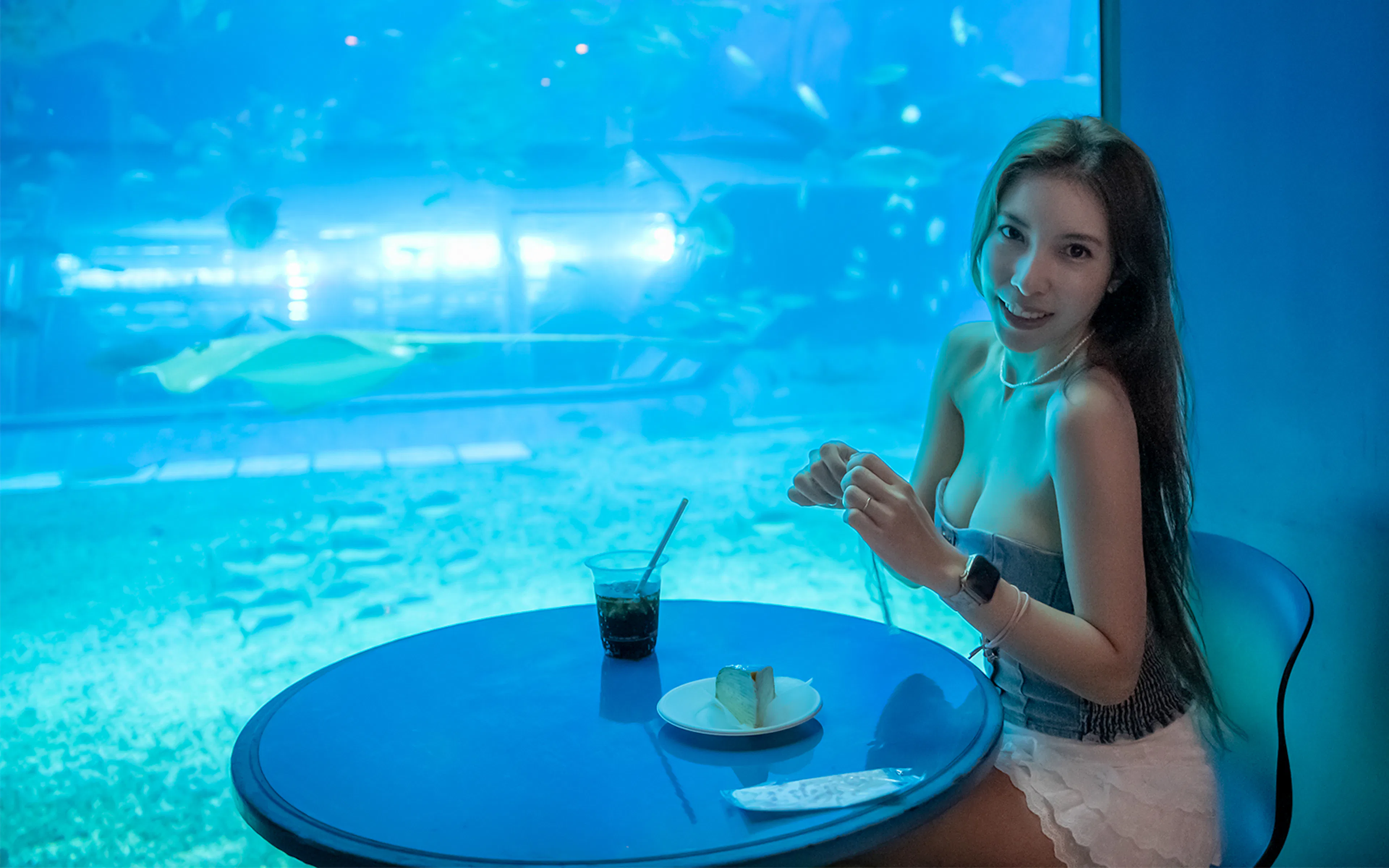 Woman dining at a cafe table with an aquarium backdrop.