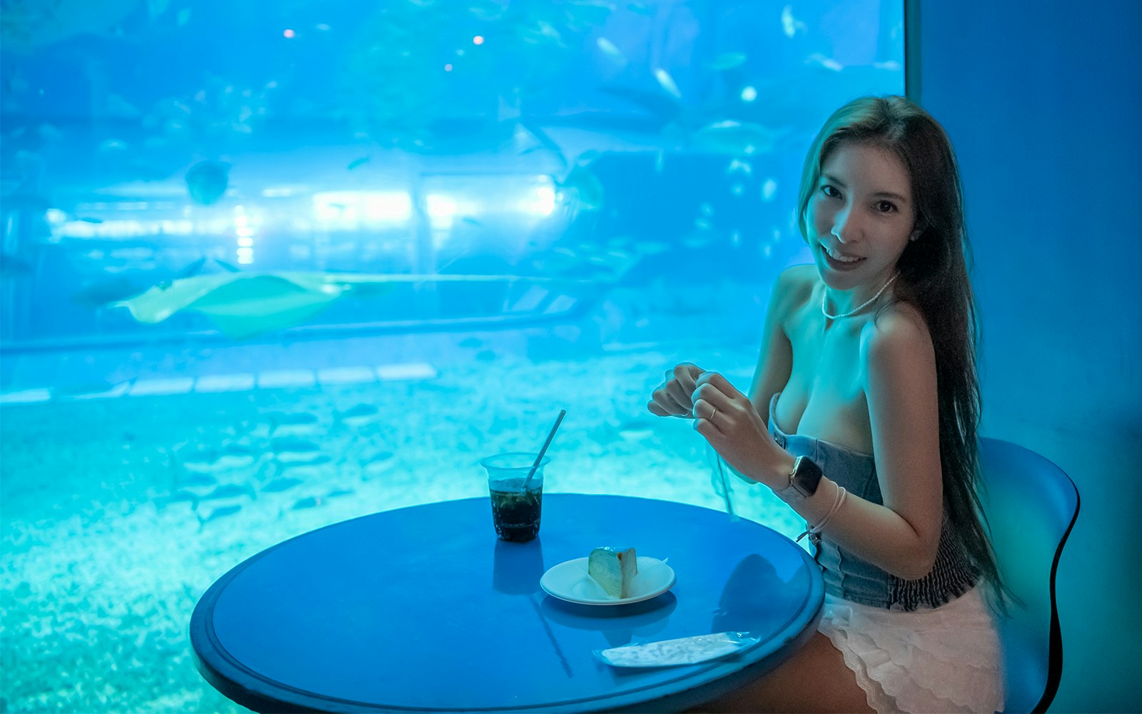 Woman dining at a cafe table with an aquarium backdrop.