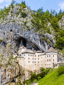 Predjama Castle built into a cliffside in Slovenia, surrounded by lush greenery.