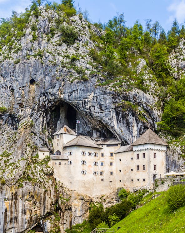 Predjama Castle built into a cliffside in Slovenia, surrounded by lush greenery.