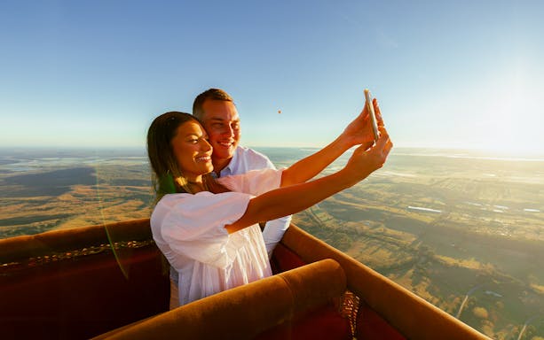 Couple taking a selfie in a hot air balloon over Gold Coast at sunrise.