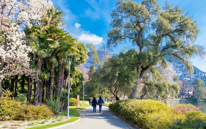 People walking along a path in Ciani Park, Lugano, surrounded by trees and greenery.
