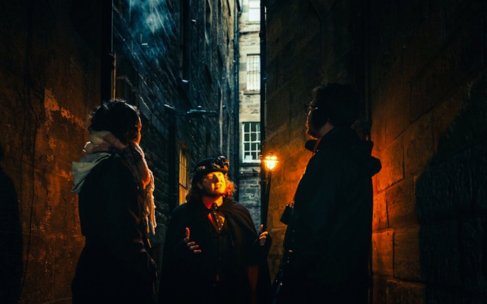 Guests on a guided tour in a dimly lit Edinburgh alleyway.