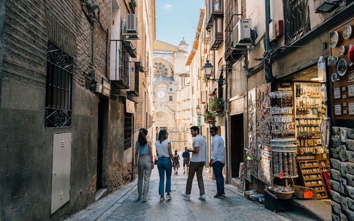 Tourist group with guide exploring narrow street in Toledo with cathedral in background.
