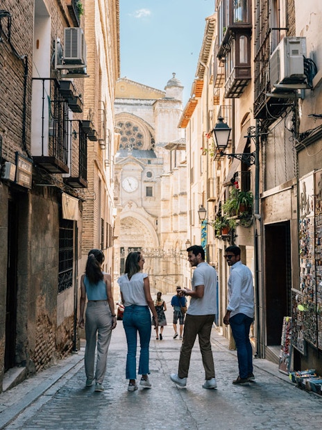 Tourist group with guide exploring narrow street in Toledo with cathedral in background.