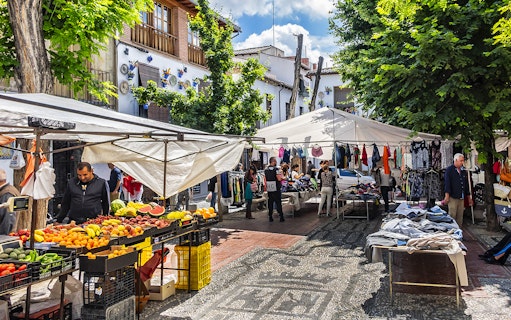Outdoor market in Albaicin, Granada with stalls selling fruits, clothes, and local crafts.