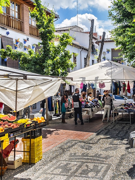 Outdoor market in Albaicin, Granada with stalls selling fruits, clothes, and local crafts.