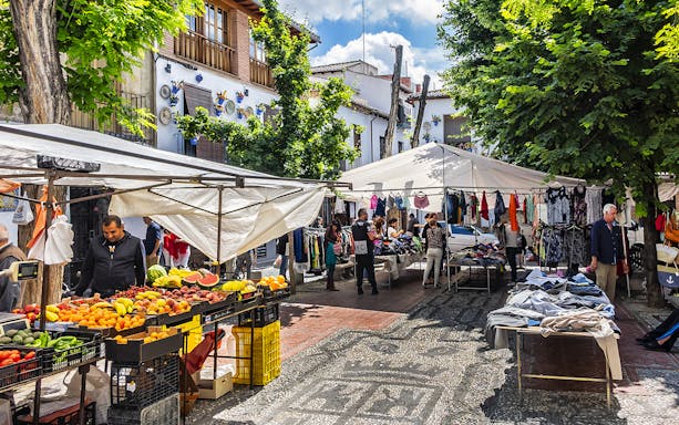 Outdoor market in Albaicin, Granada with stalls selling fruits, clothes, and local crafts.