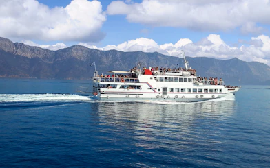 Ferry with passengers sailing near Mykonos, Greece, with mountainous backdrop.