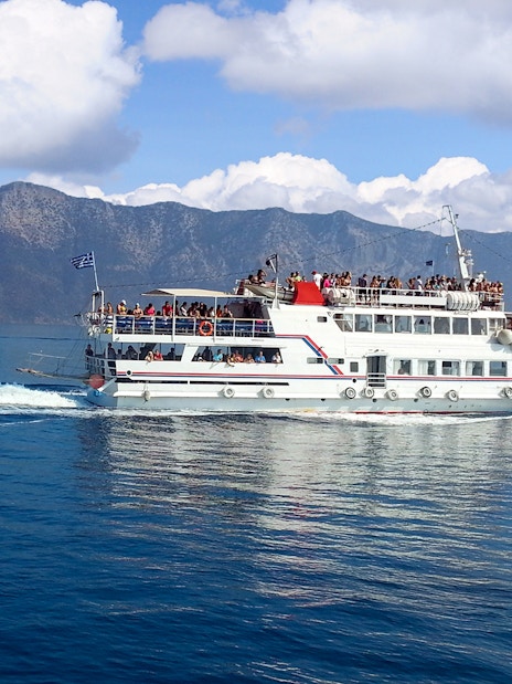 Ferry with passengers sailing near Mykonos, Greece, with mountainous backdrop.
