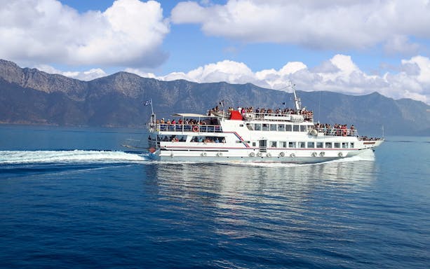 Ferry with passengers sailing near Mykonos, Greece, with mountainous backdrop.