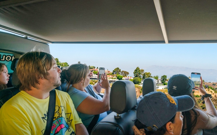 Tourists on Hollywood Sightseeing bus capturing views of celebrity homes, Los Angeles.