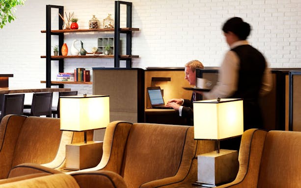 Plaza Premium Lounge seating area with guest working on laptop, Terminal 4, London Heathrow Airport.