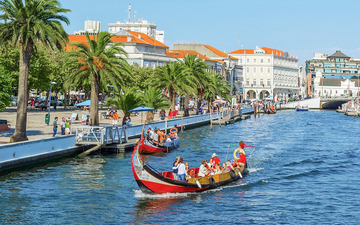 Moliceiro boat cruising along the canal in Aveiro, Portugal, with tourists enjoying the view.