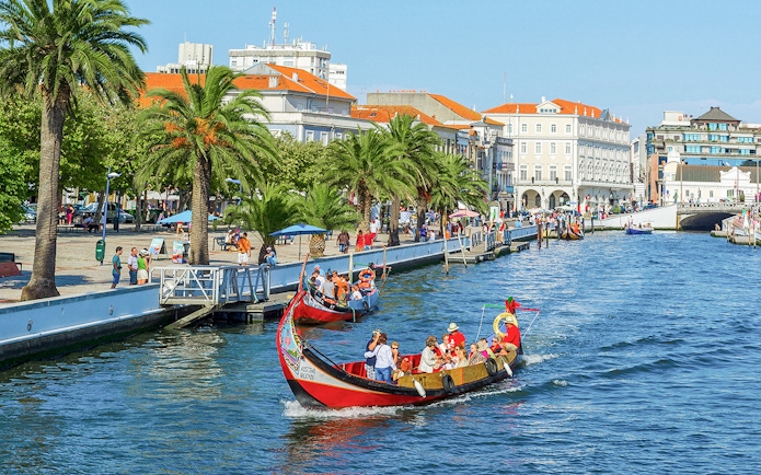 Moliceiro boat cruising along the canal in Aveiro, Portugal, with tourists enjoying the view.