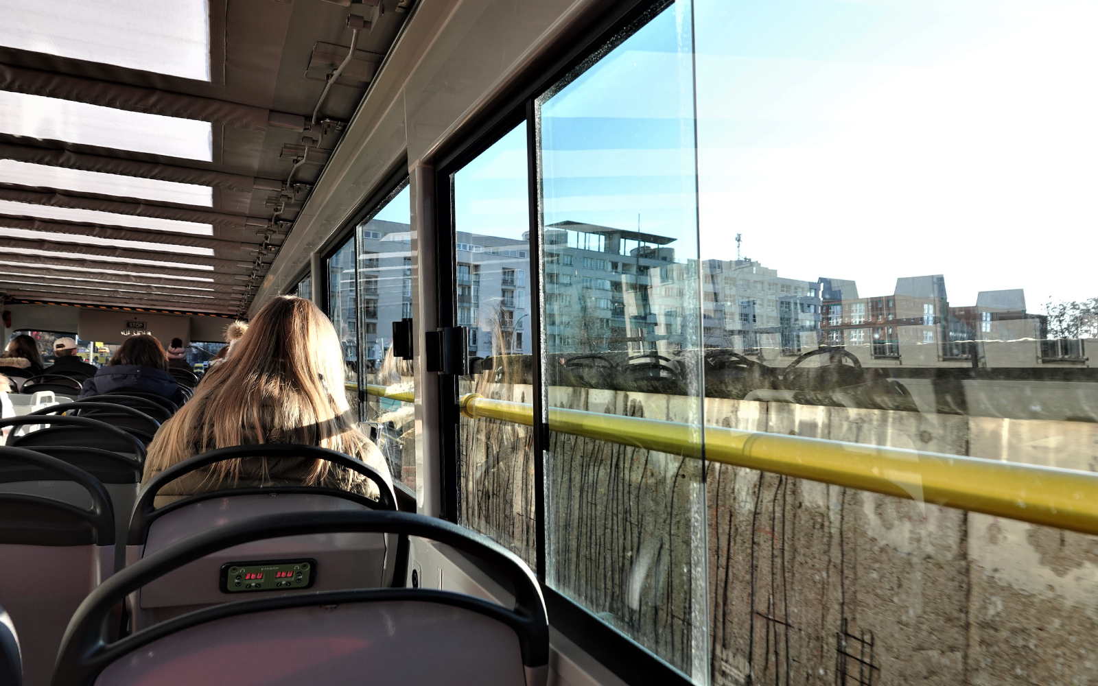 Passengers on Berlin hop-on hop-off bus tour viewing cityscape through windows.