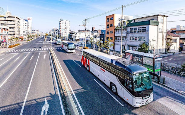 Kansai Airport shared shuttle van driving on a sunny day in an urban area.