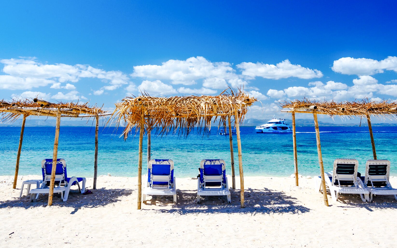 Lounge chairs under thatched shades on a sandy beach, South Sea island, Fiji.