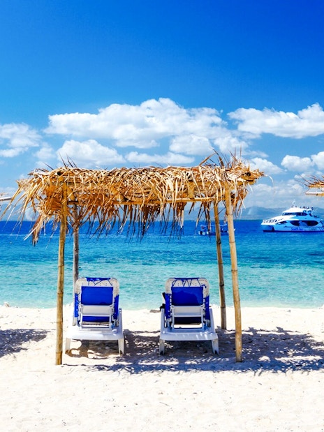 Lounge chairs under thatched shades on a sandy beach, South Sea island, Fiji.