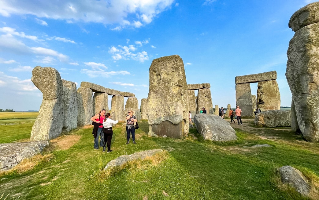 Visitors walking among Stonehenge stones under a blue sky in Wiltshire, England.