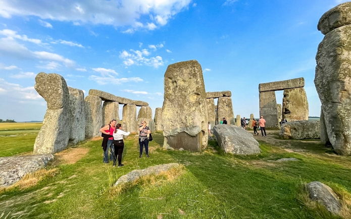 Visitors walking among Stonehenge stones under a blue sky in Wiltshire, England.