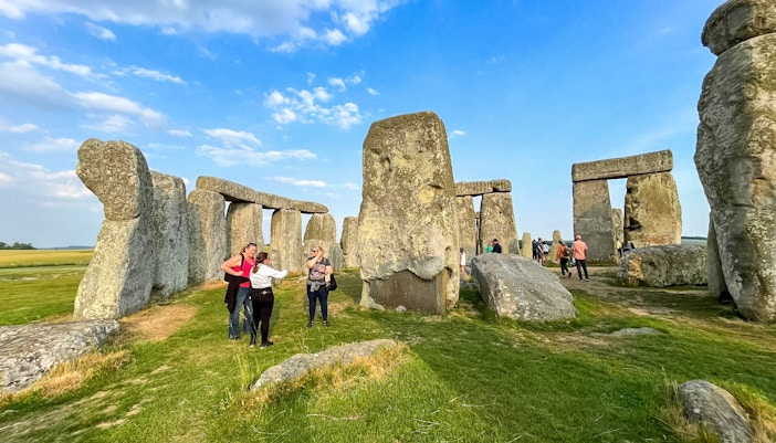 Visitors walking among Stonehenge stones under a blue sky in Wiltshire, England.