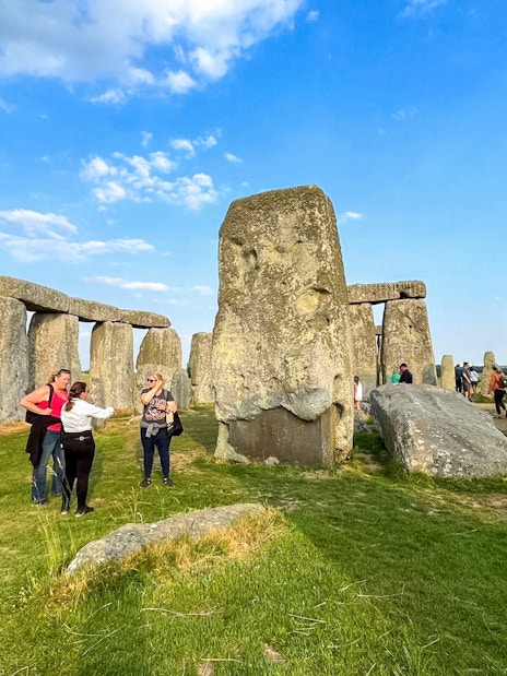 Visitors walking among Stonehenge stones under a blue sky in Wiltshire, England.