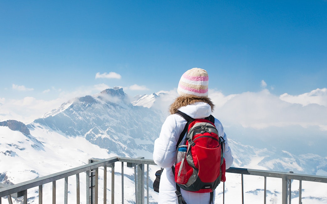 Woman with backpack overlooking snowy peaks at Mt. Titlis summit.