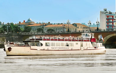 Cruise boat on Bordeaux river with cityscape and bridge in background.