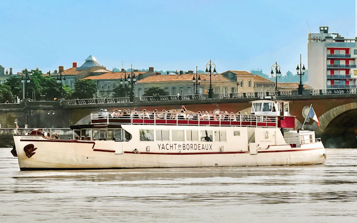 Cruise boat on Bordeaux river with cityscape and bridge in background.