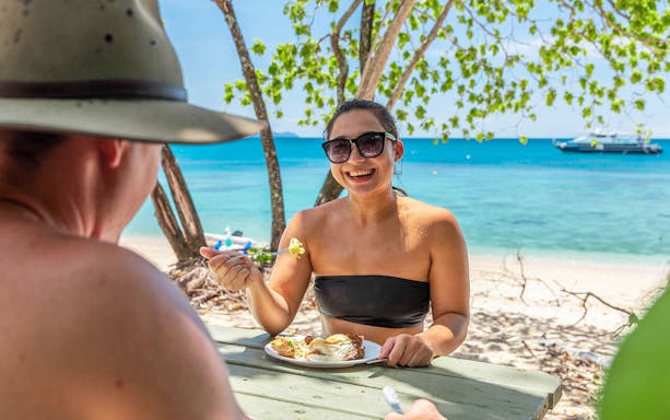 Couple dining on Frankland Islands beach with ocean view.