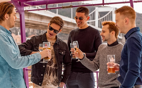 Group enjoying drinks on a Budapest evening cruise with bridge in background.
