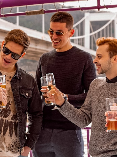 Group enjoying drinks on a Budapest evening cruise with bridge in background.