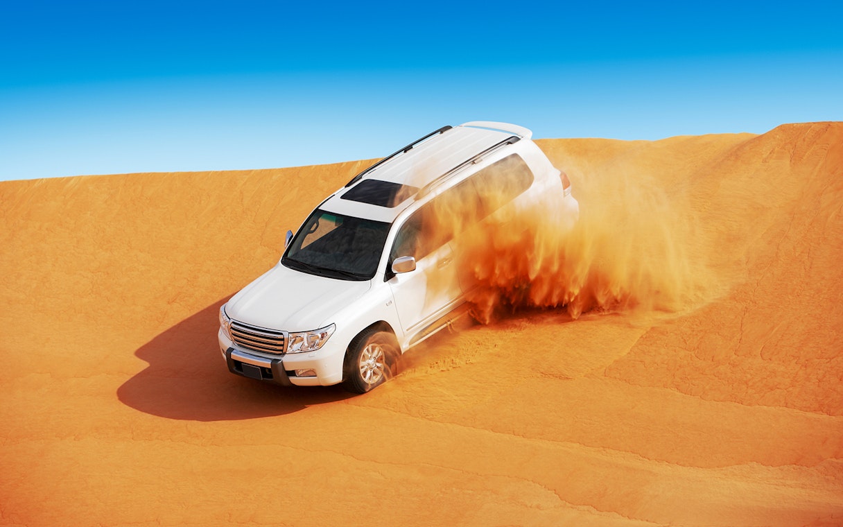 SUV driving through sand dunes in Abu Dhabi desert.