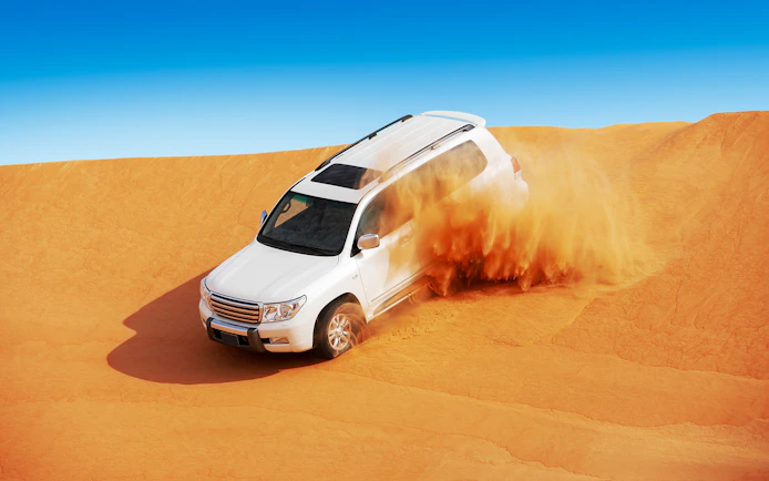 SUV driving through sand dunes in Abu Dhabi desert.