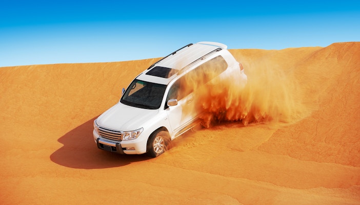 SUV driving through sand dunes in Abu Dhabi desert.