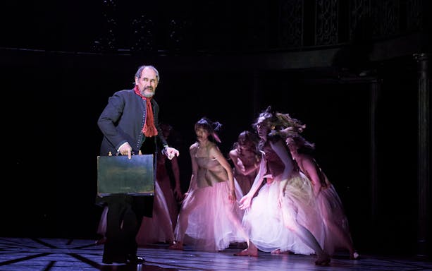 Man holding briefcase on stage with dancers in flowing dresses, Dr Semmelweis performance.