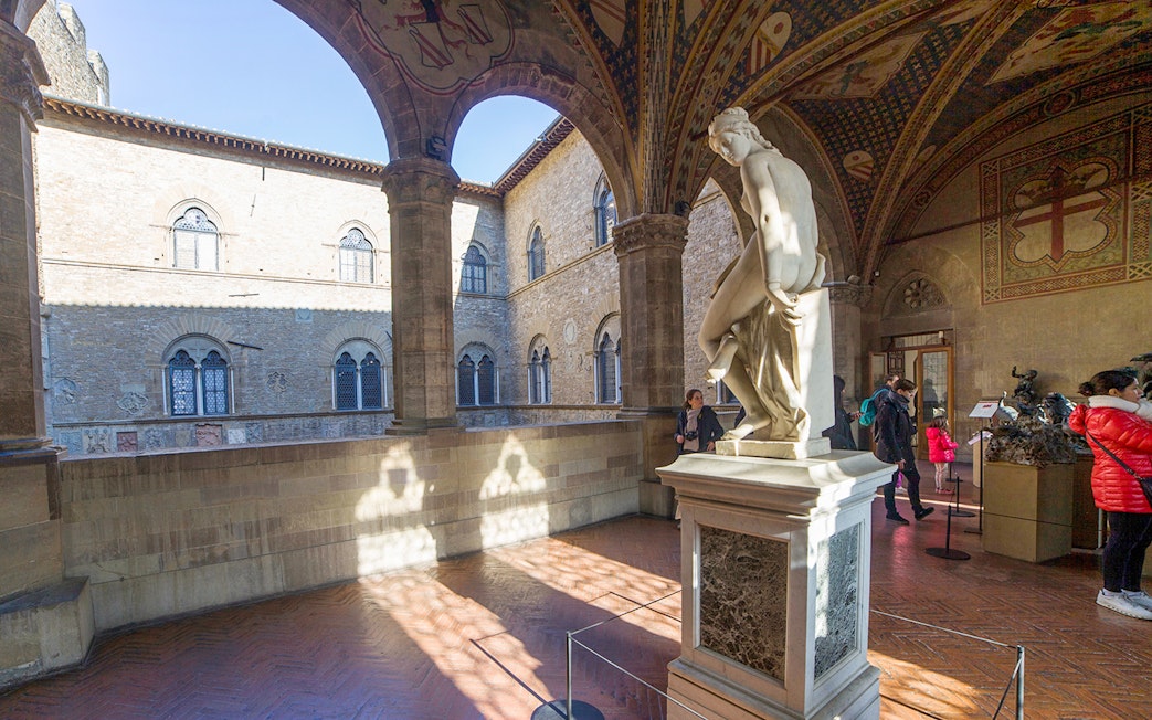 Statue in the courtyard of Museo del Bargello, Florence, with visitors exploring exhibits.