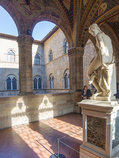 Statue in the courtyard of Museo del Bargello, Florence, with visitors exploring exhibits.