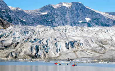 Kayakers paddling near a glacier with mountain backdrop on Norris Adventure tour.