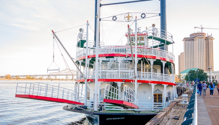 New Orleans paddle steamer cruising the Mississippi River with city skyline in the background.
