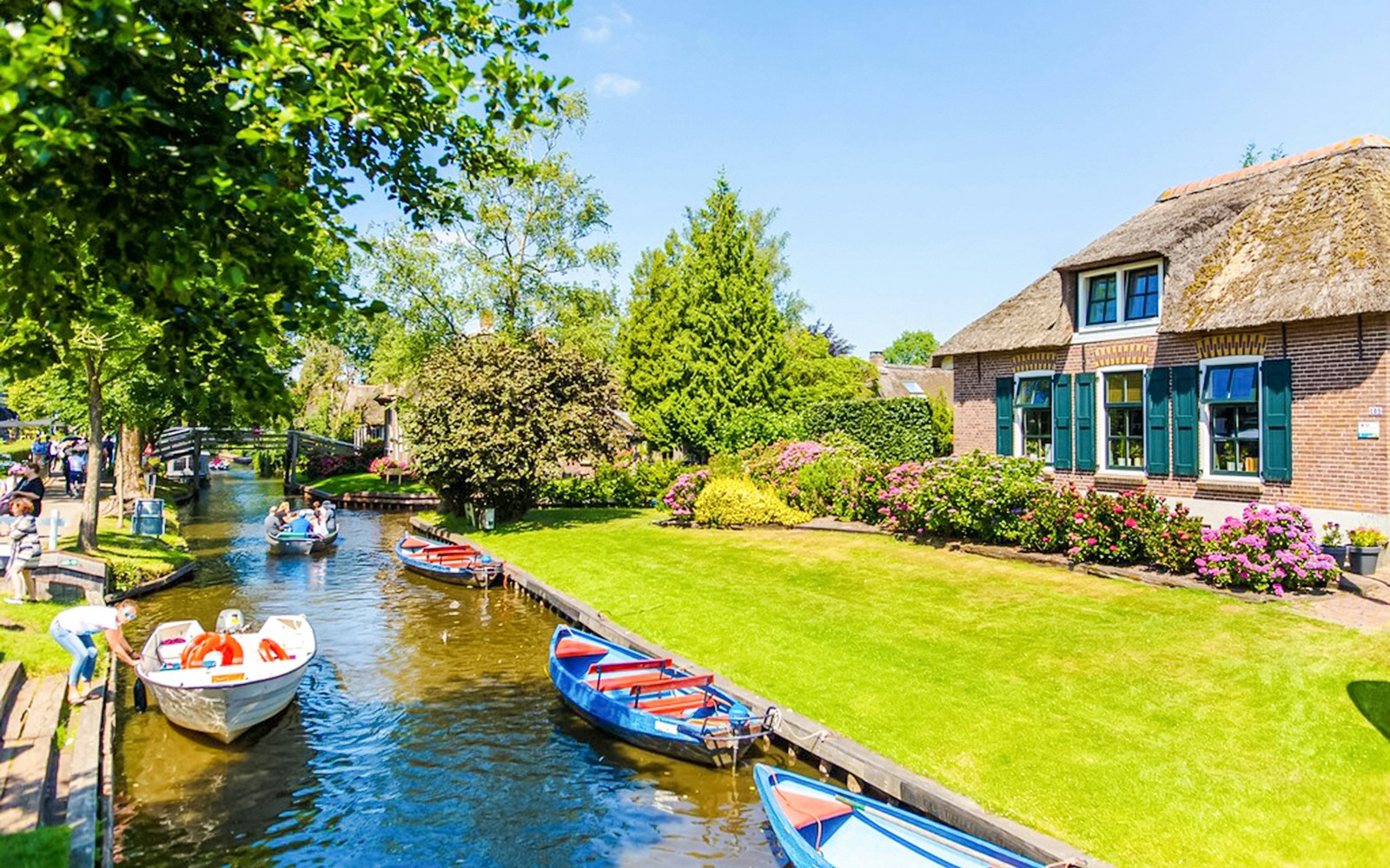 Boats on a canal in Giethoorn with traditional houses and lush gardens.