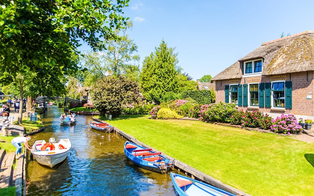 Boats on a canal in Giethoorn with traditional houses and lush gardens.