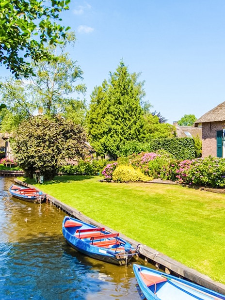 Boats on a canal in Giethoorn with traditional houses and lush gardens.