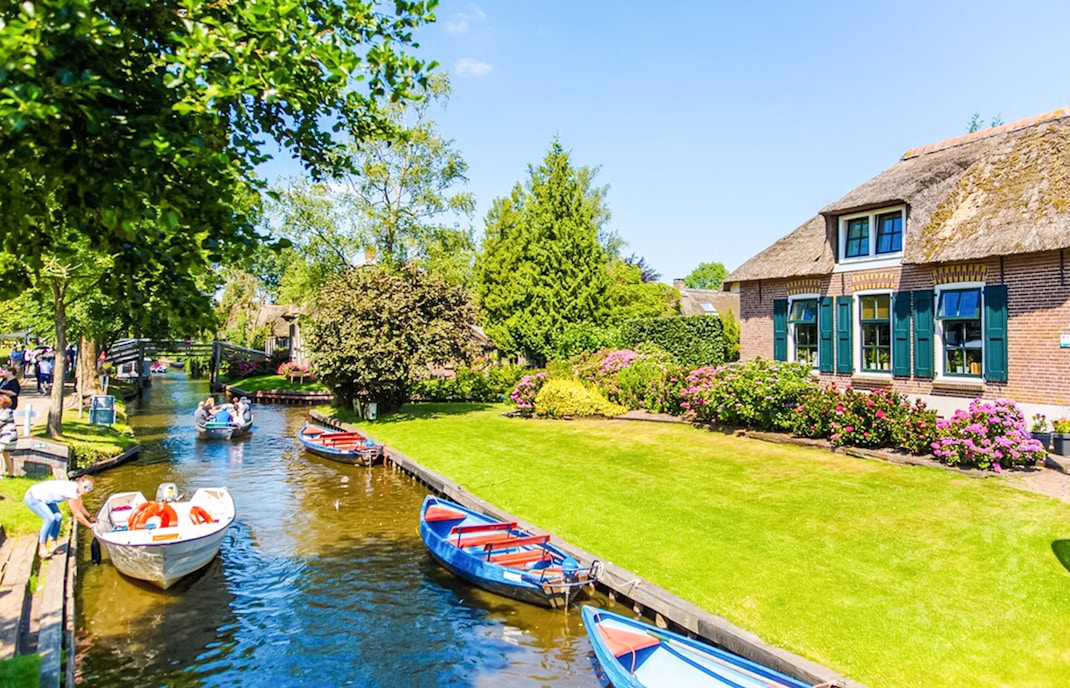 Giethoorn canal with tour boat and traditional thatched-roof houses in the Netherlands.