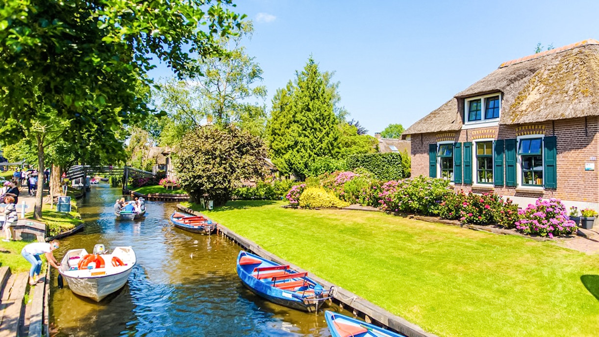 Boats on a canal in Giethoorn with traditional houses and lush gardens.