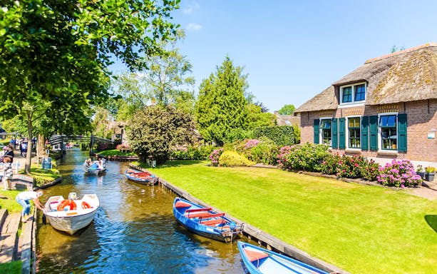Boats on a canal in Giethoorn with traditional houses and lush gardens.