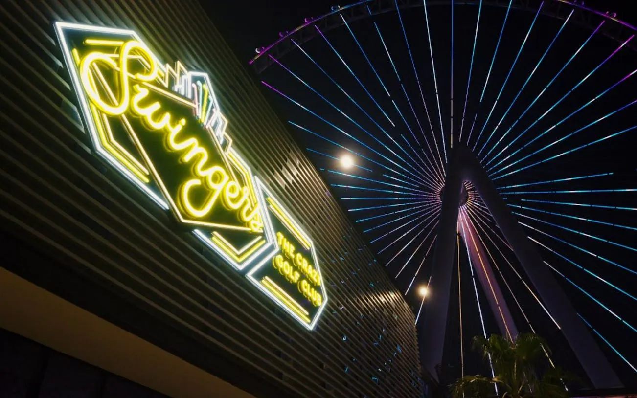 Swingers mini golf club neon sign with Ferris wheel in the background at night.