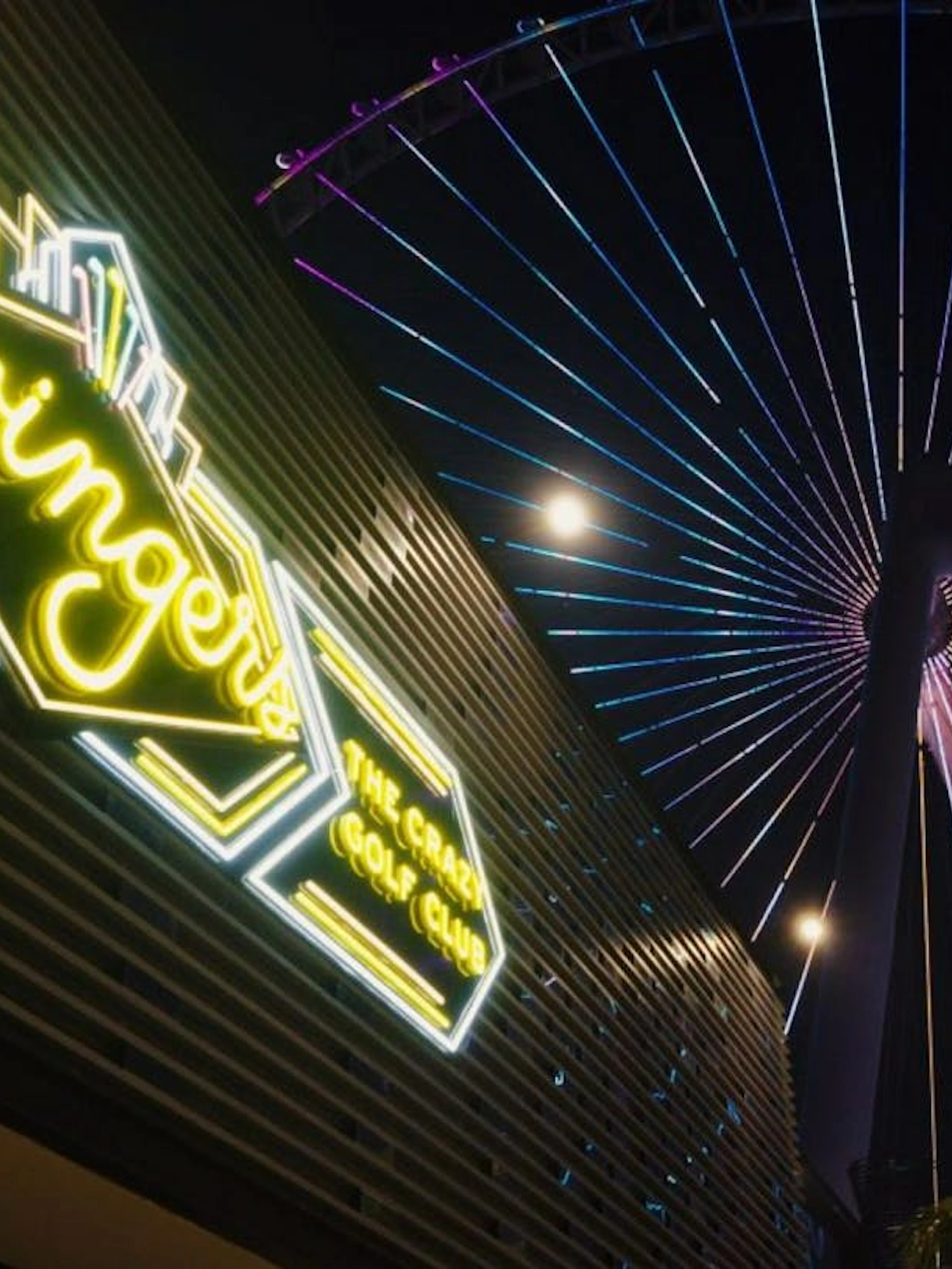 Swingers mini golf club neon sign with Ferris wheel in the background at night.