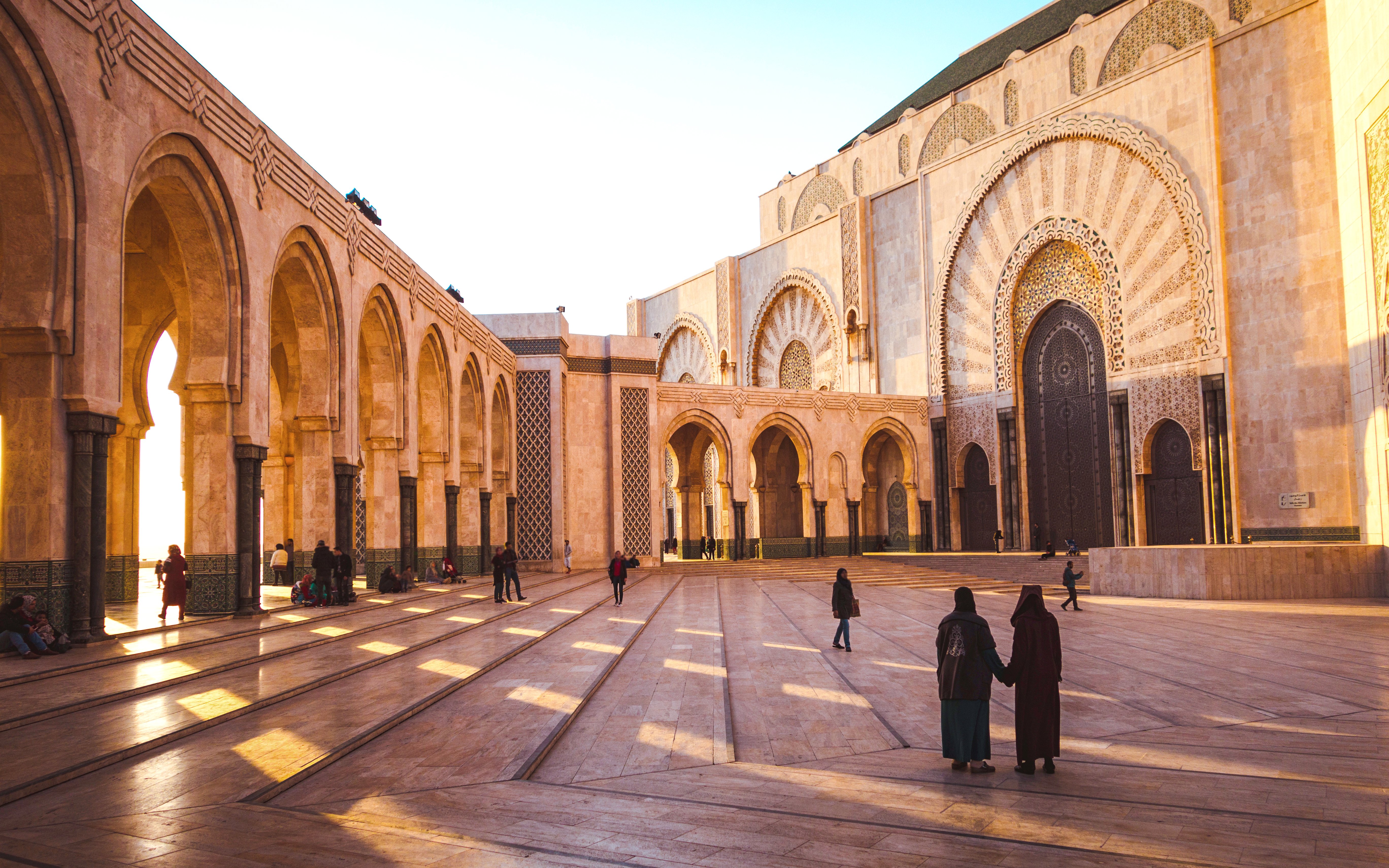 Ornate brass door and arches of Hassan II Mosque, Casablanca, Morocco, with people in courtyard.